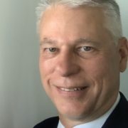 A photo of a smiling man with white hair in a suit.