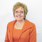 A photo of a woman with blonde/light brown hair, wearing an orange suit and glasses.