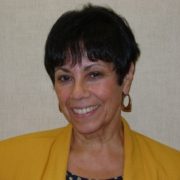 Photo of a woman with short, dark brown hair and yellow suit jacket.